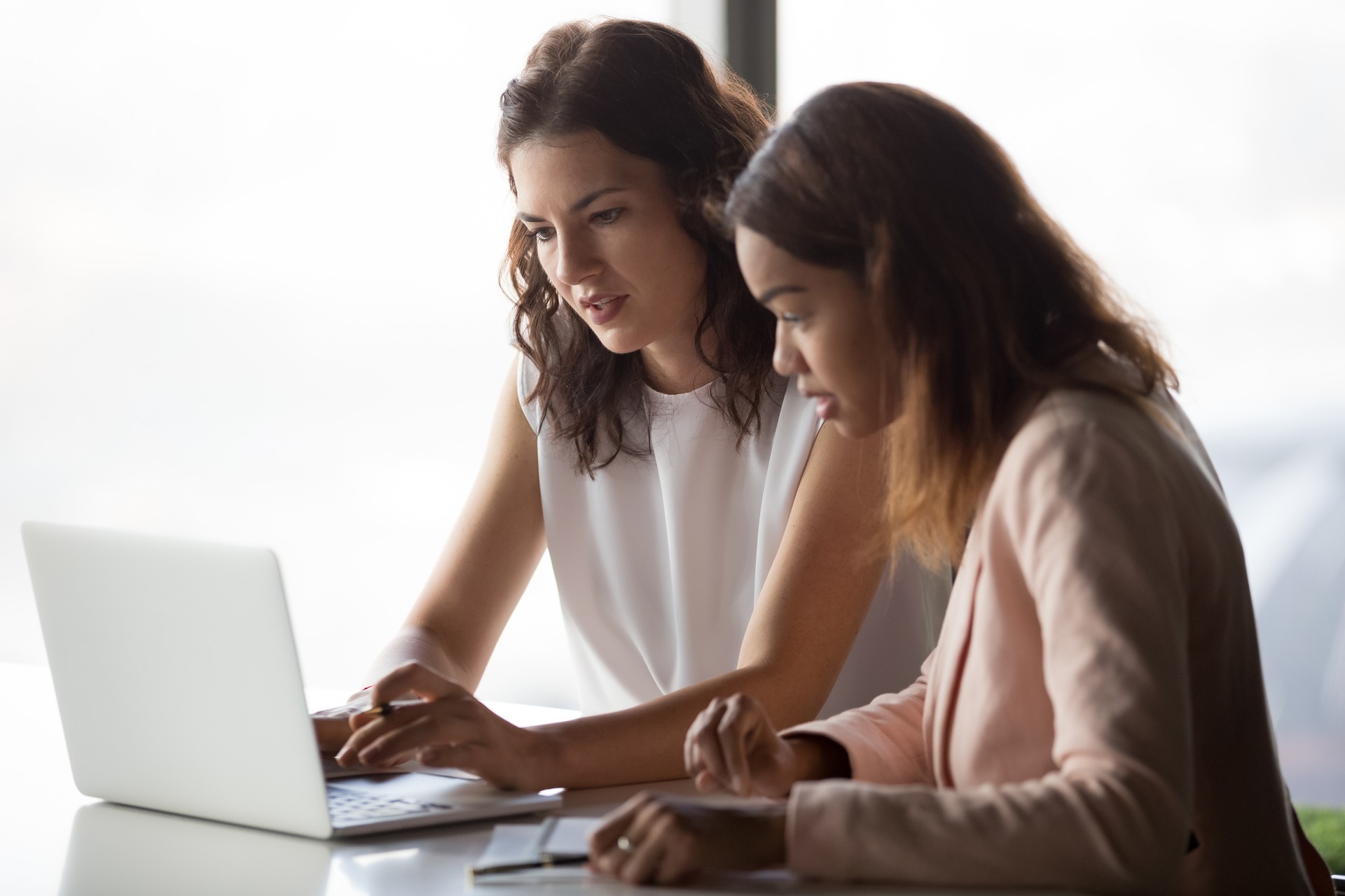 Femmes d’affaires diverses graves discutant en ligne projet regardant ensemble portable